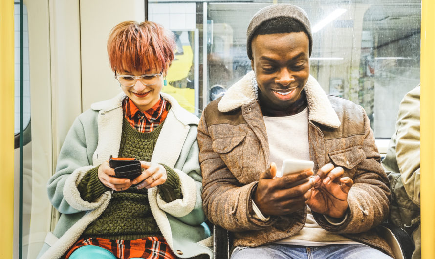 Two friends on the subway checking their mobile phones and smiling