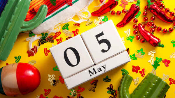 Mexican fiesta and Cinco de Mayo party concept with calendar set on May 5th, jalapeno pepper necklace, maracas, cactus and traditional rug covered in sombrero shaped confetti on yellow background stock photo