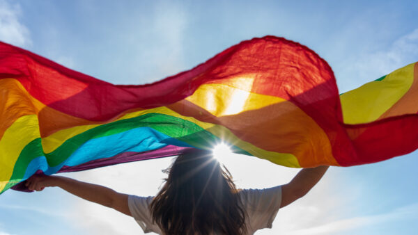Person looks to sky with rainbow flag