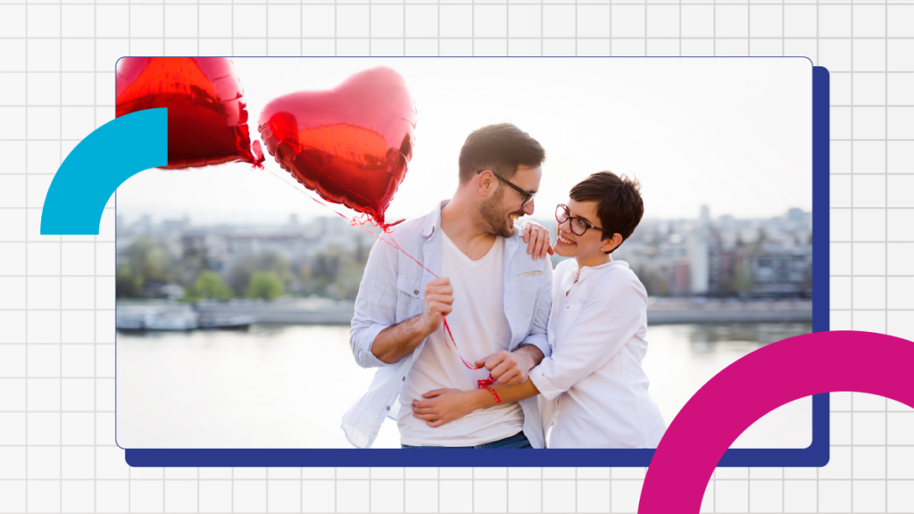 Couple stand on a bridge with two red foil heart shaped ballons