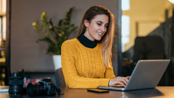 Woman in yellow jumper smiles as she works on a laptop