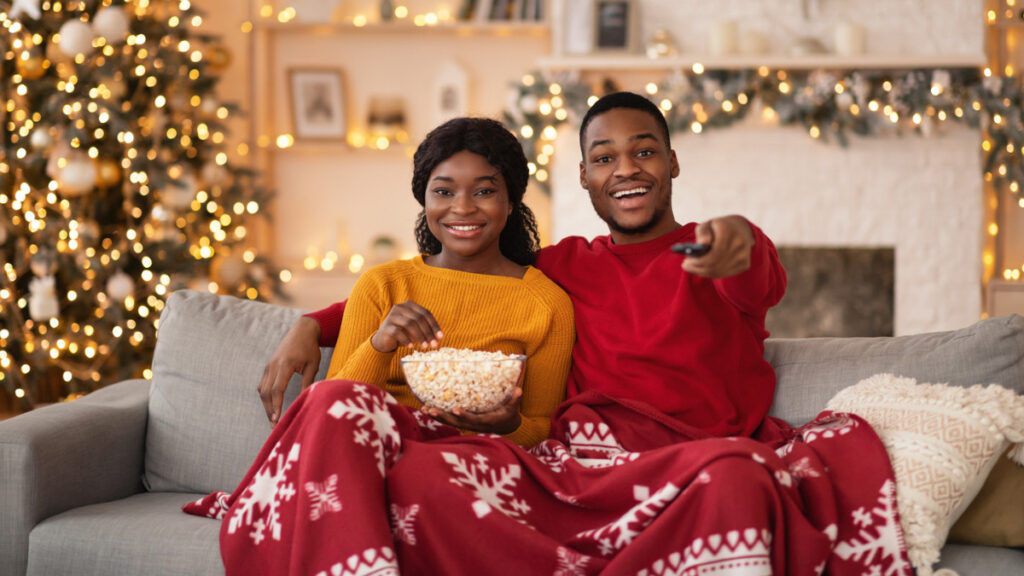 Couple sitting on sofa with Christmassy background, pressing play on tv remote